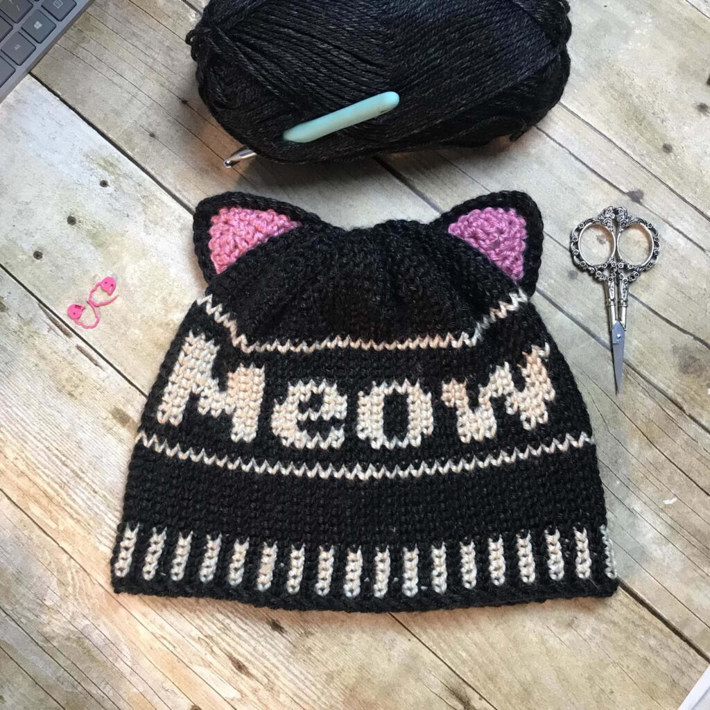 Kitty Cat Crochet Beanie black and white on table with pink kitty ears by stardust gold crochet