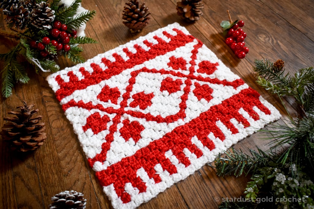 Red and White C2C Nordic Vines Afghan Square on brown hardwood floor with pine cones and holly