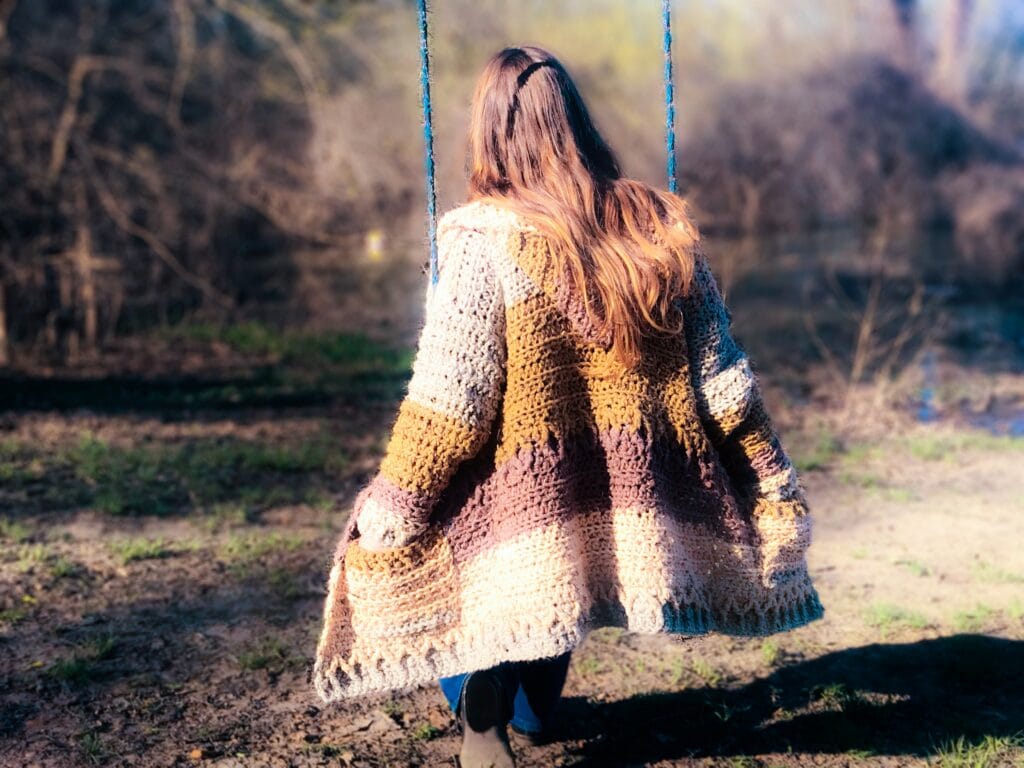 Tasha Margette on a swing with back facing the camera, wearing the kirra crochet cardigan pattern