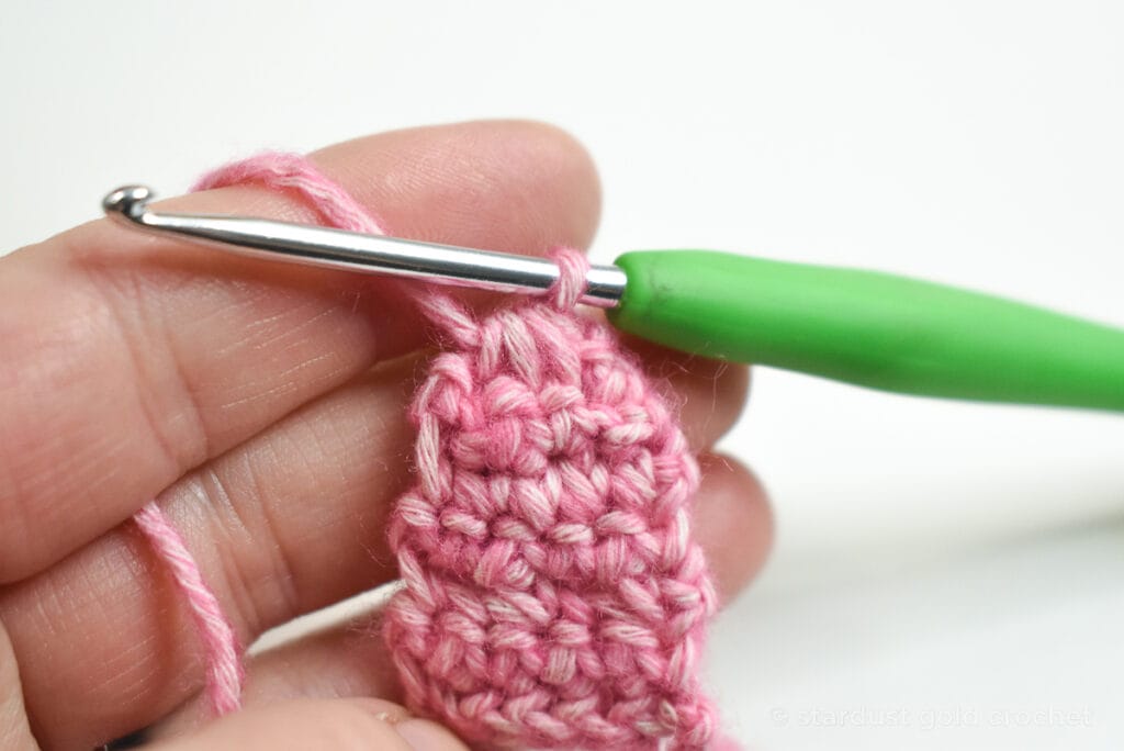 pink yarn with green crochet hook, step 11 of crochet bookmark pattern