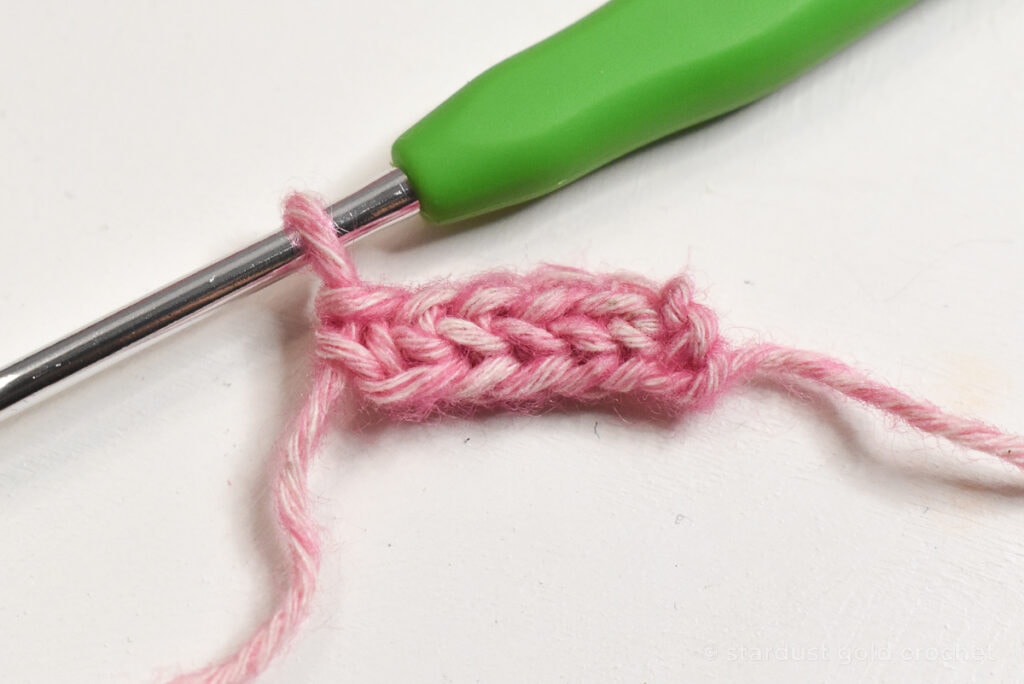 pink yarn with green crochet hook, step 1 of crochet bookmark pattern
