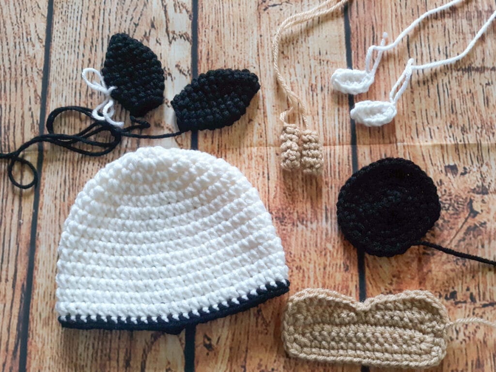 black and white crochet cow beanie pattern assembly pieces on table