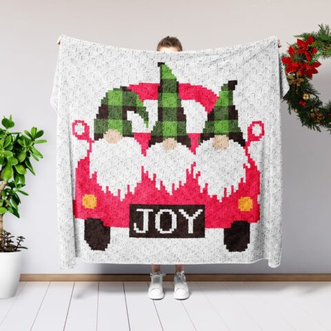 woman holding c2c crochet gnome blanket against white background with a christmas wreath and plant