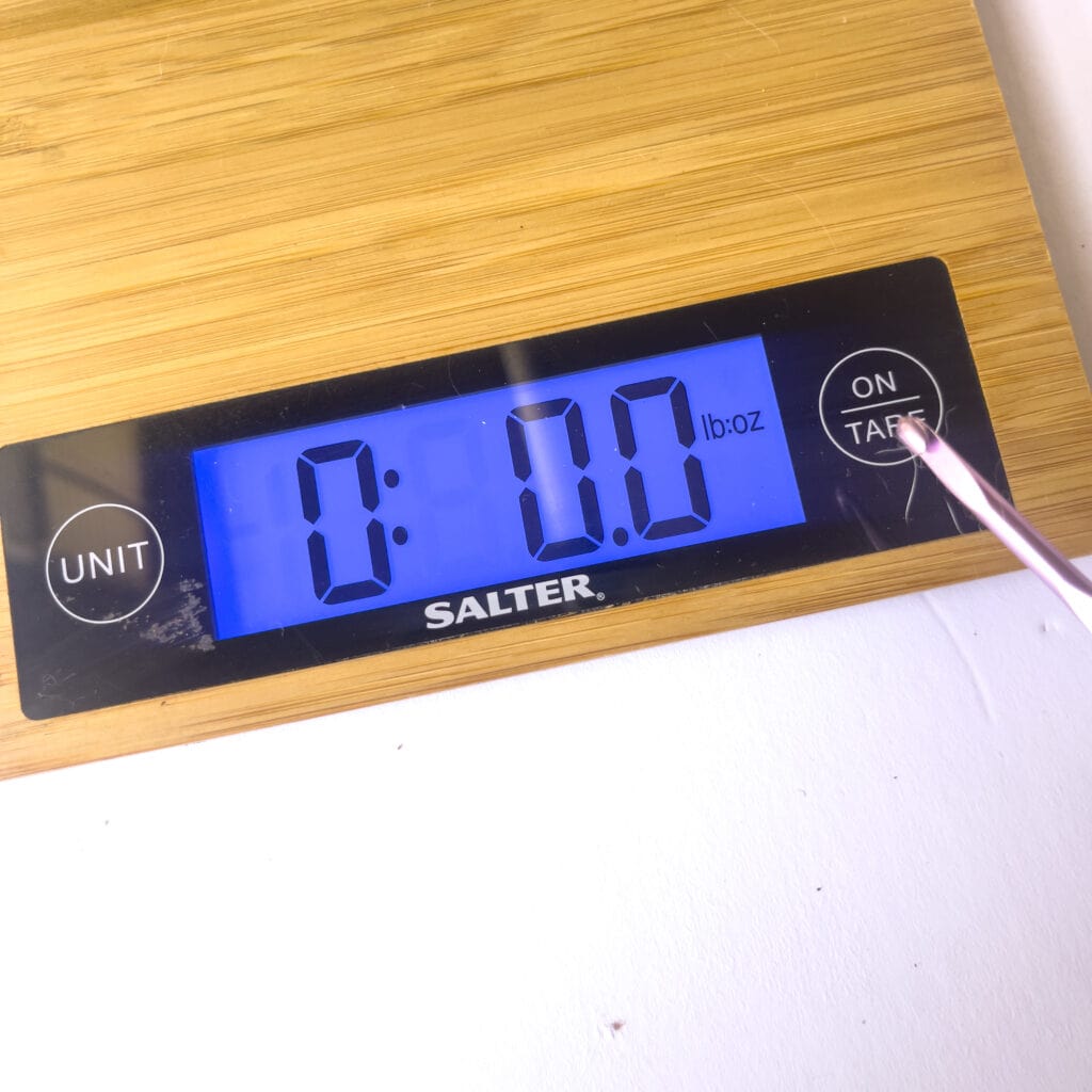 Up close of a digital scale with a crochet hook pushing the tare button