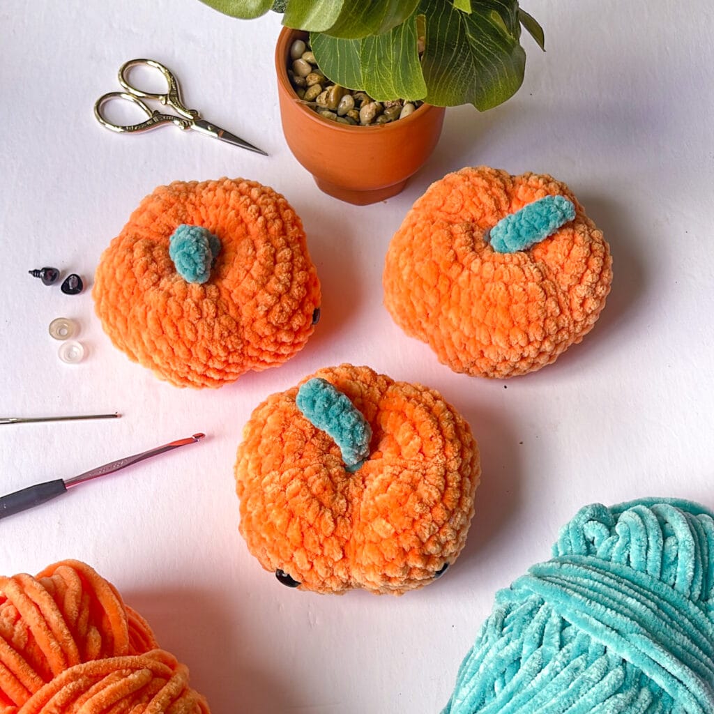 crochet amigurumi pumpkins with notions on table with a plant