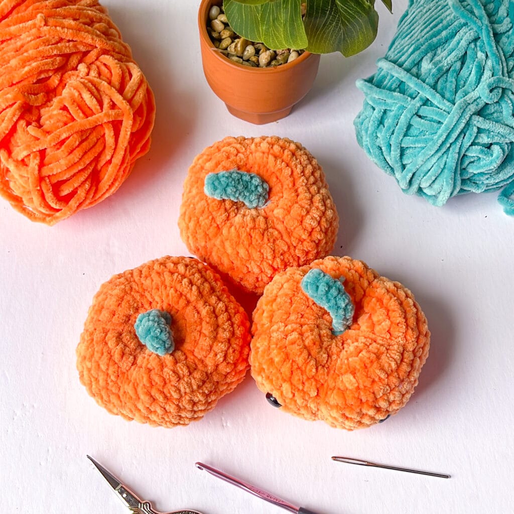 crochet amigurumi pumpkins with notions on table with a plant